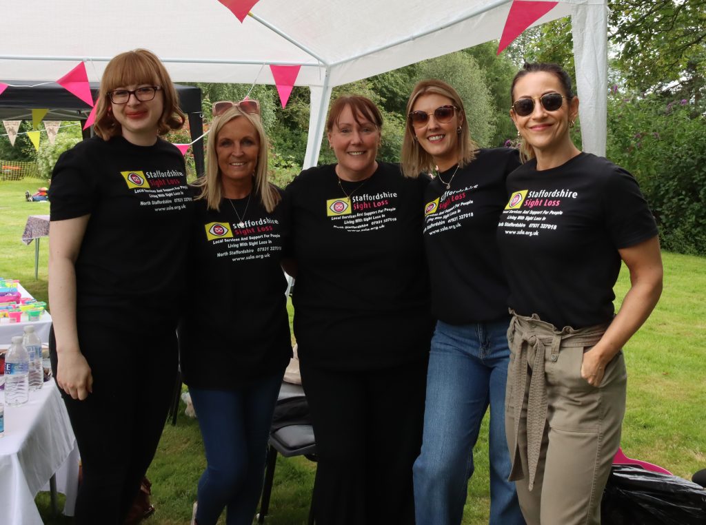 This image shows a group of 5 female volunteers proudly wearing their black staffordshire Sight Loss Tshirts. They all have big smiles on their faces, and look ready for the day.